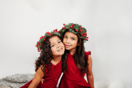 Two sisters in holly headpieces pose for christmas photo