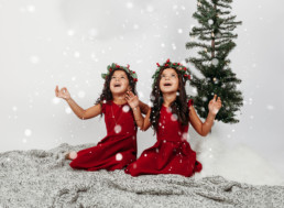 Two children dressed in christmas outfits play in snow