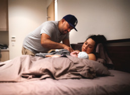 Photo of father looking down at newborn baby and mother post birth in a birth center