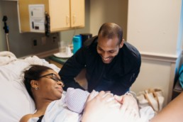 Photo of father smiling down at newborn baby and mother post birth in a hospital birth