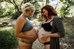 Two pregnant mothers face each other while holding and looking at their bellies