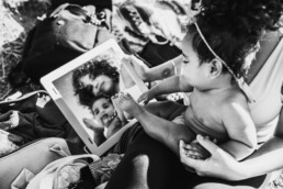 Black and white image of mother and baby looking into a mirror, their reflection shows their faces