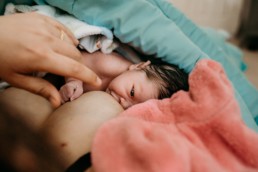 Newborn baby gazes into mother's eyes while nursing during homebirth. Both are covered in blankets