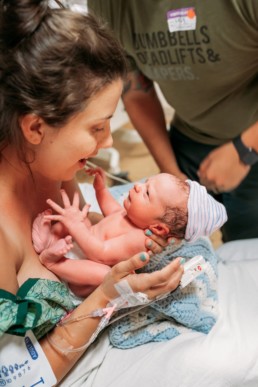 Mom in hospital gown hold newborn baby. Mom and baby look at each other in the eyes.