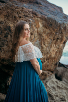 Pregnant women next to dramatic rock looking away from camera while holding belly