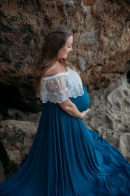 Pregnant woman holds belly while gazing down at belly in dramatic blue skirt.
